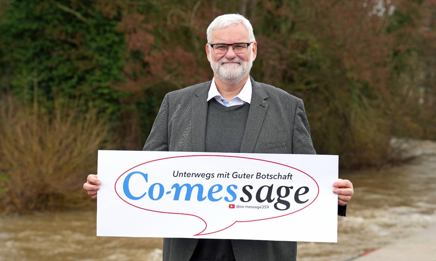 Ein Mann blickt in die Kamera. In den Händen hält er ein Plakat mit der Aufschrift 'Co-message'