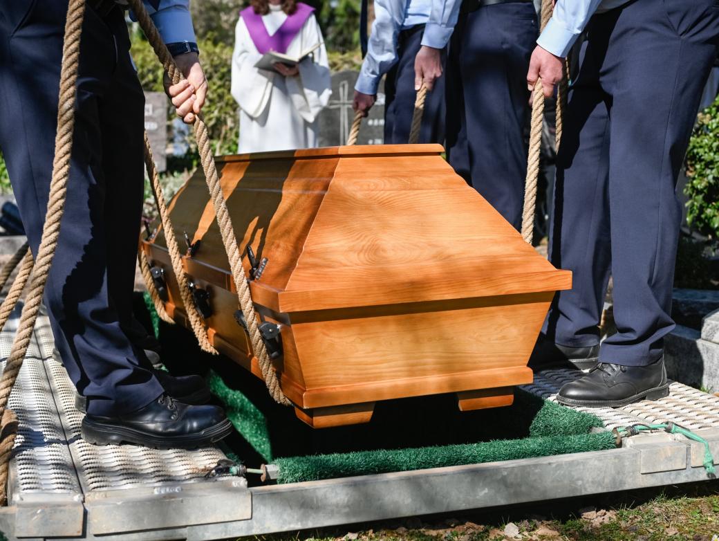 Männer lassen einen Sarg in ein vorbereitetes Grab sinken