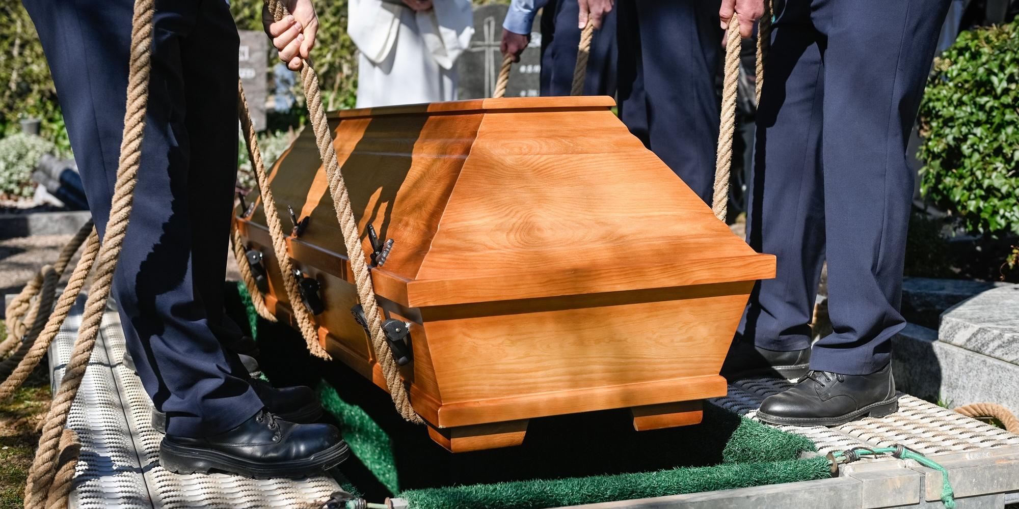 Männer lassen einen Sarg in ein vorbereitetes Grab sinken