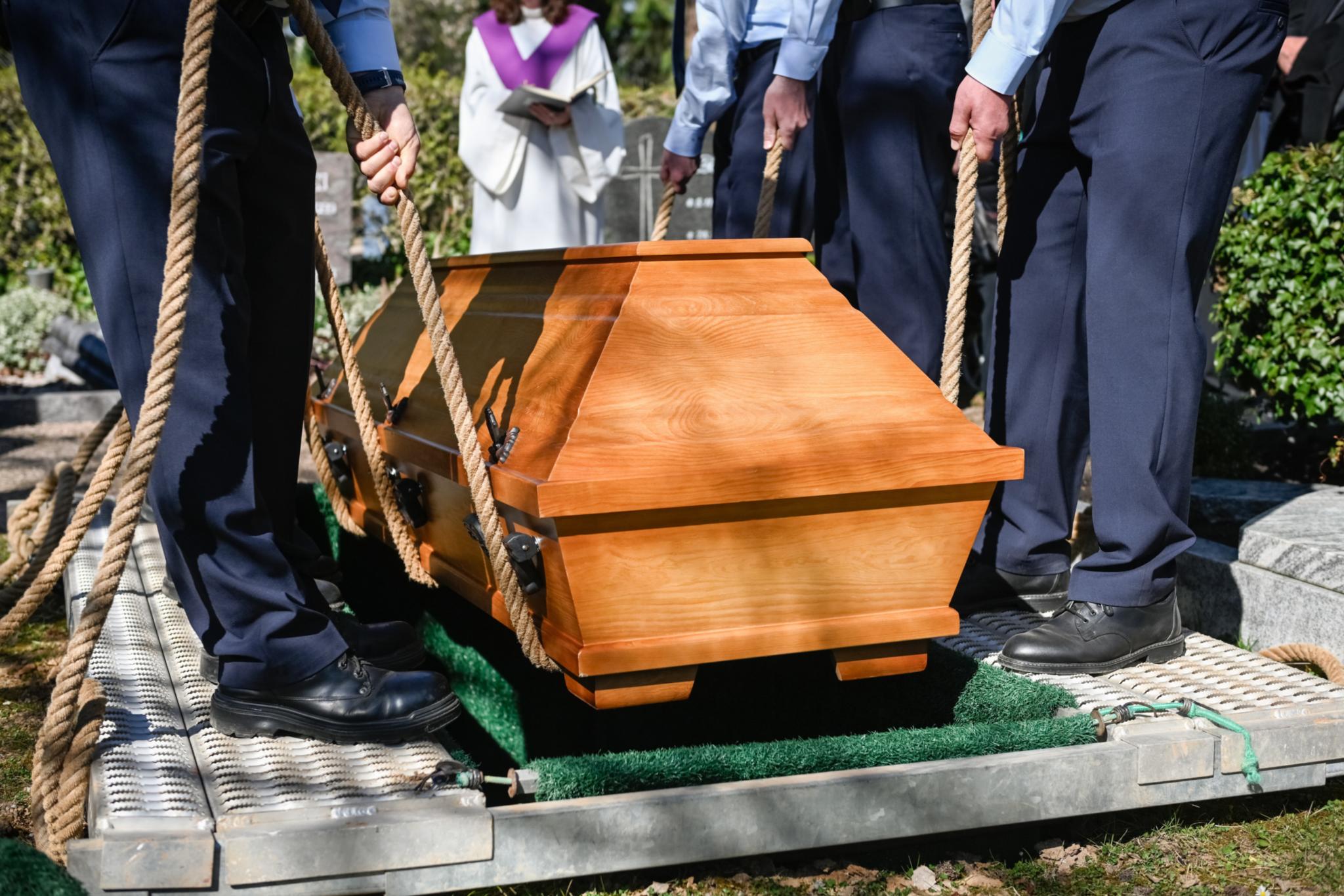 Männer lassen einen Sarg in ein vorbereitetes Grab sinken