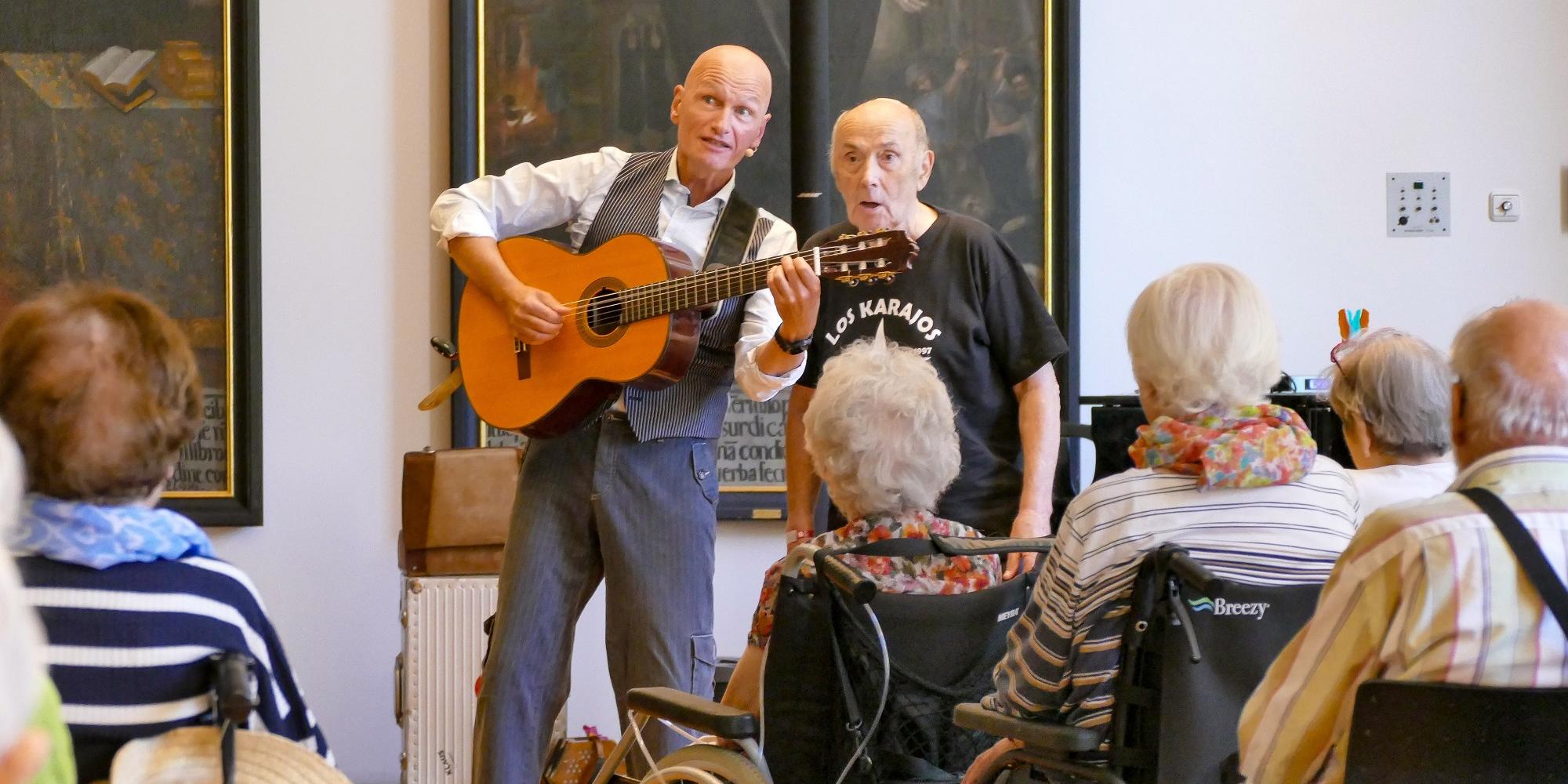Ein Mann mit Gitarre singt mit einem anderen Mann vor Publikum