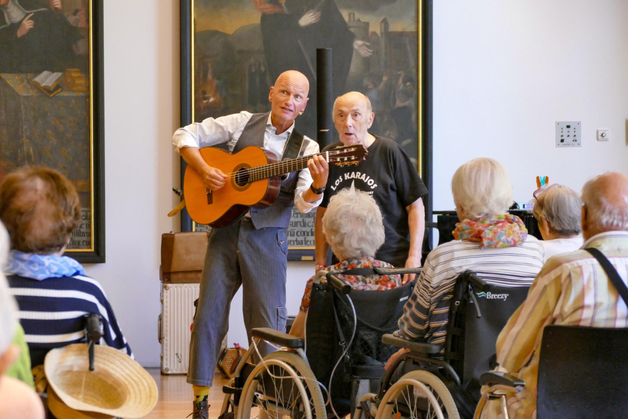 Ein Mann mit Gitarre singt mit einem anderen Mann vor Publikum