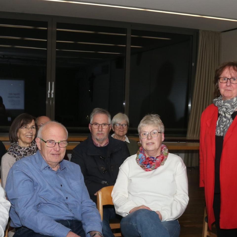 Dekan Jörg Schuh und Pastoralreferentin Susanne Moeckel-Lamberty neben einer Gruppe sitzender Menschen stehend.