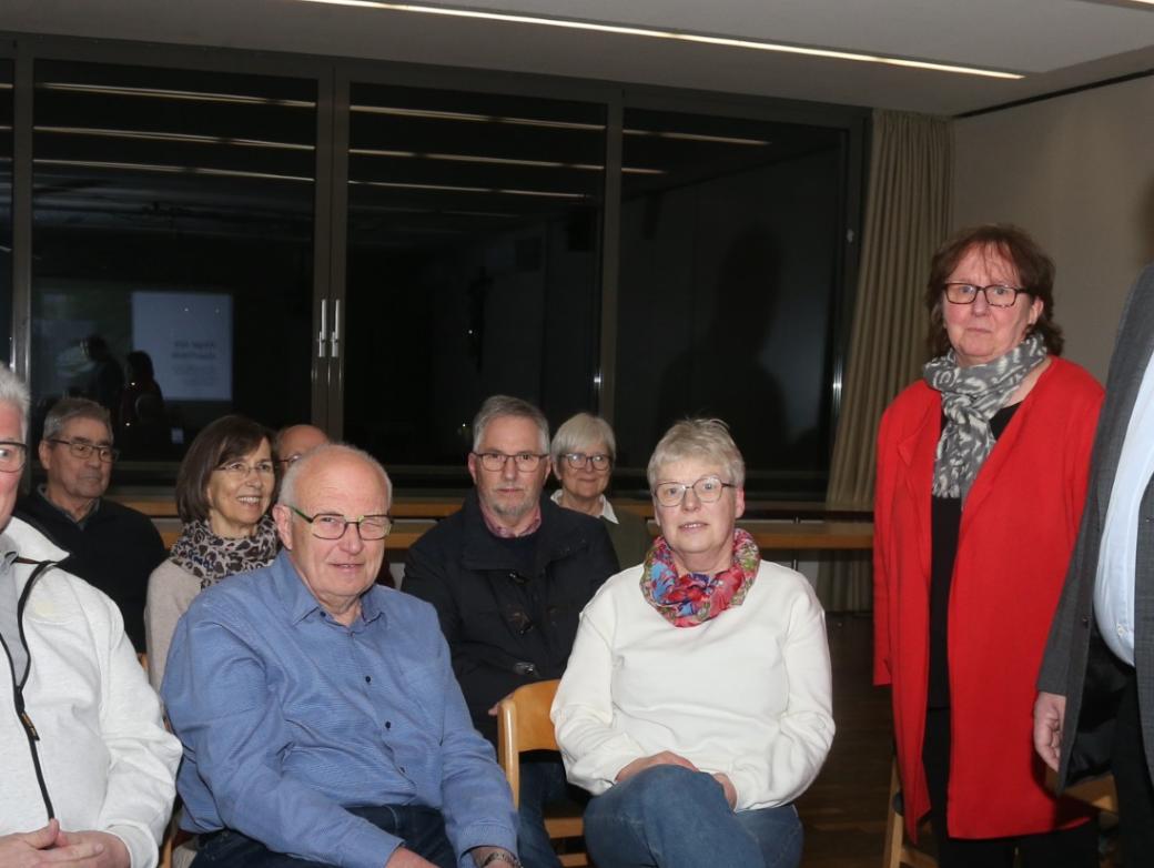 Dekan Jörg Schuh und Pastoralreferentin Susanne Moeckel-Lamberty neben einer Gruppe sitzender Menschen stehend.