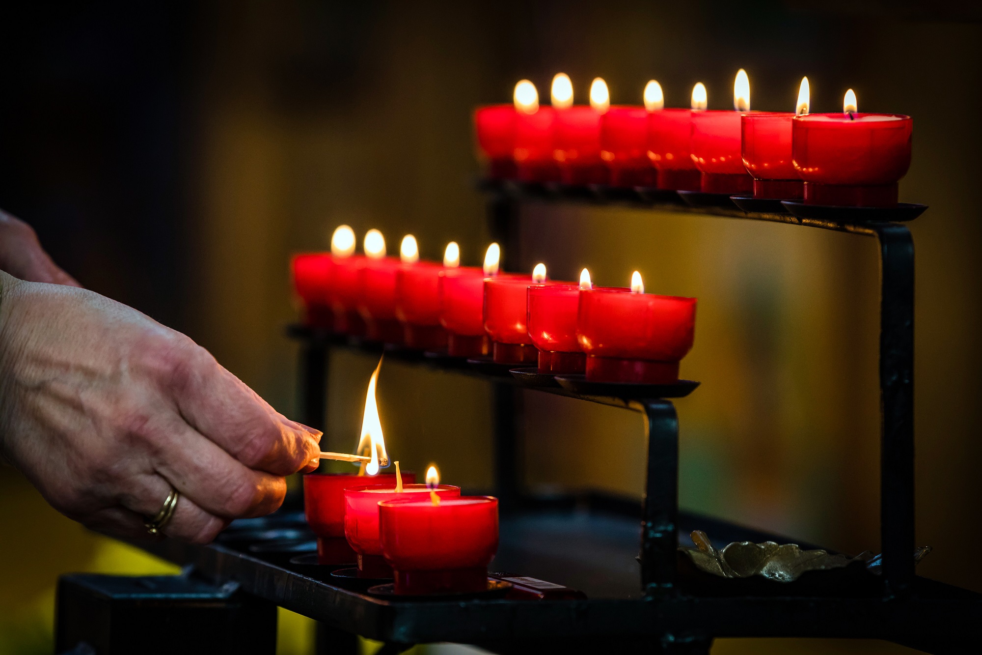 Eine Person entzündet eine Kerze auf einer Kerzenstation in einer Kirche.