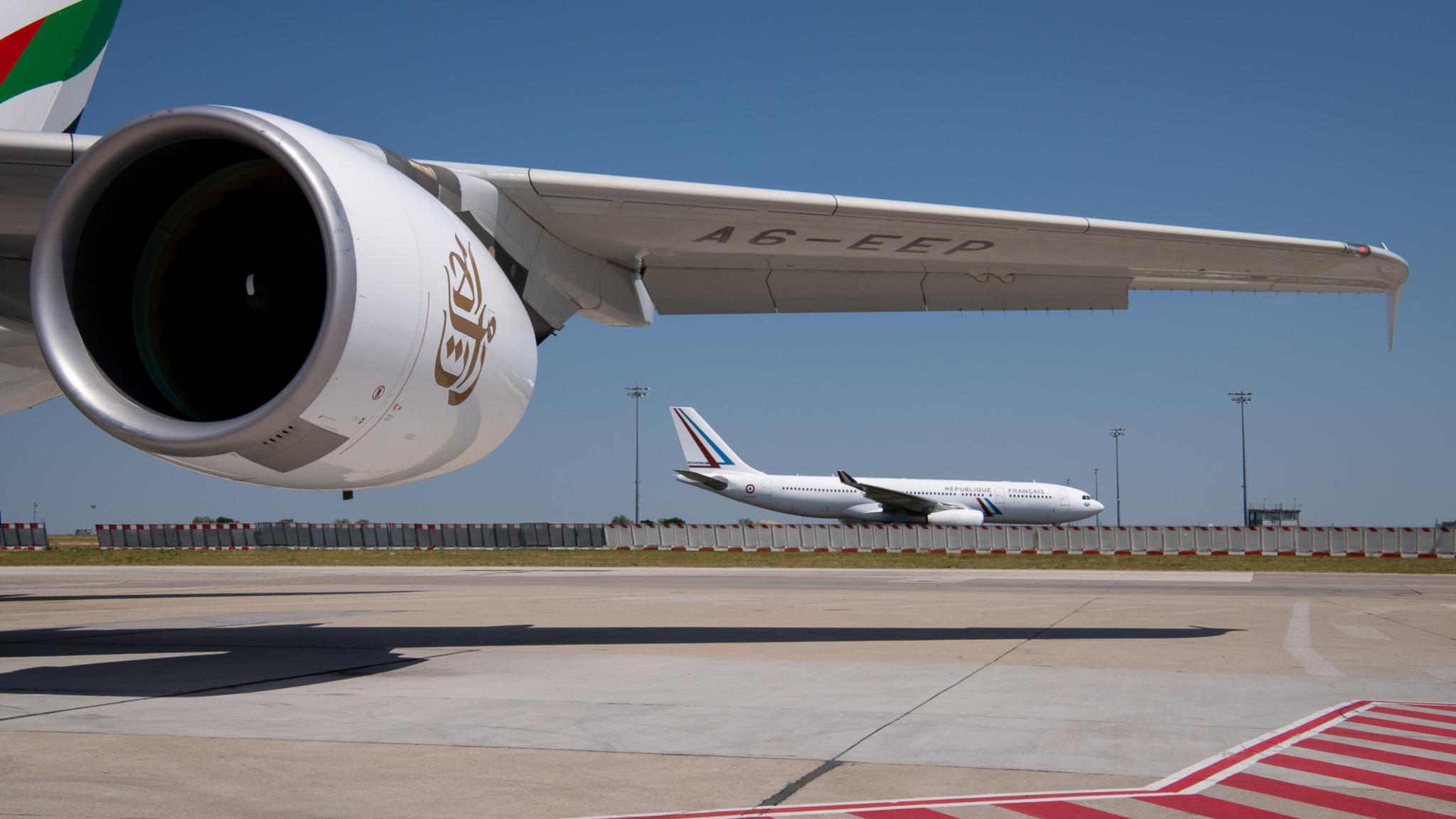 Tragfläche eines Flugzeugs, im Hintergrund ein weiteres Flugzeug auf einem Flughafen