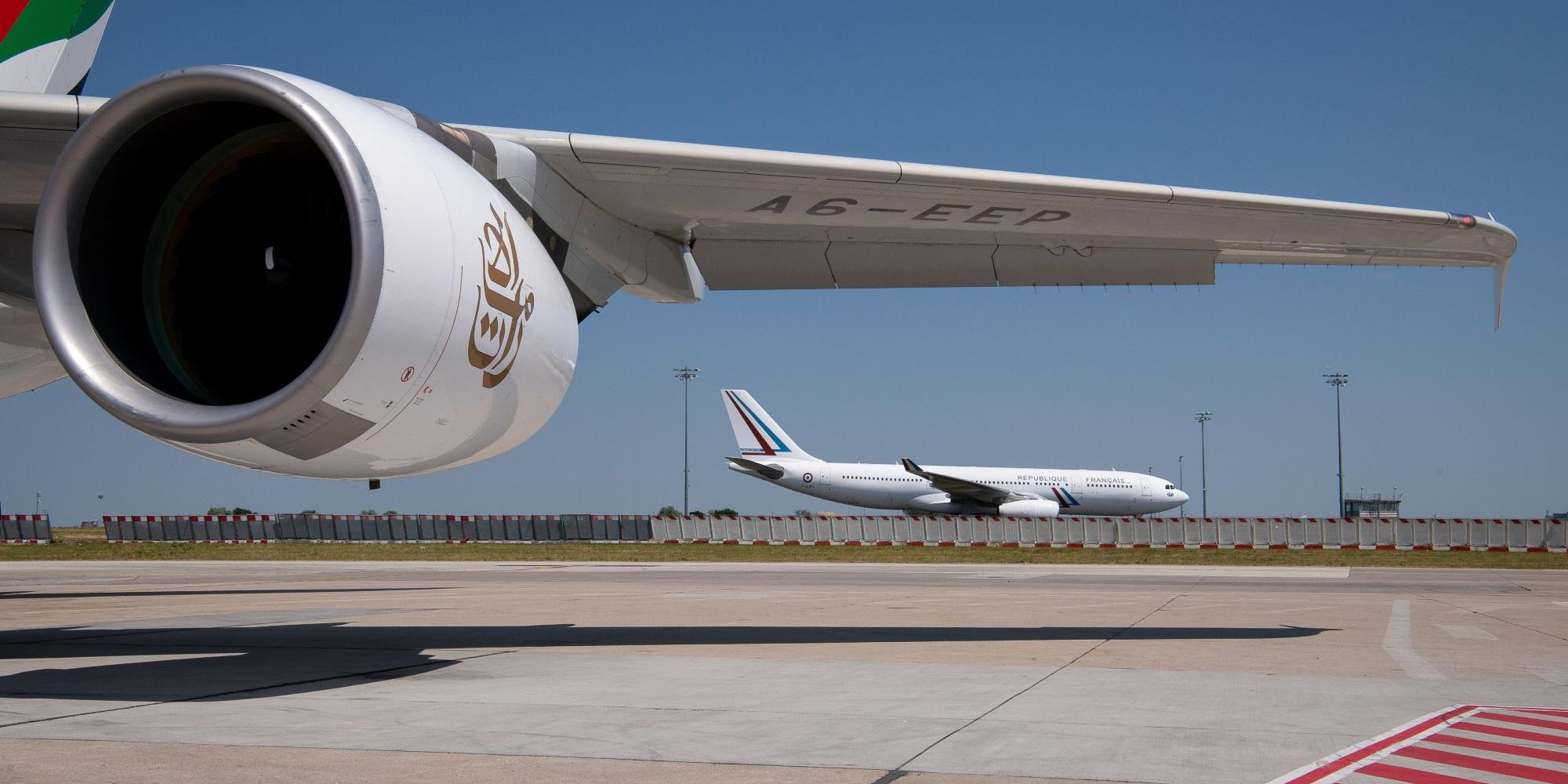 Tragfläche eines Flugzeugs, im Hintergrund ein weiteres Flugzeug auf einem Flughafen