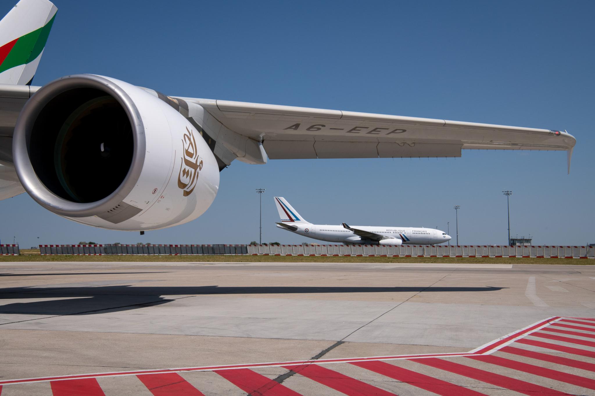 Tragfläche eines Flugzeugs, im Hintergrund ein weiteres Flugzeug auf einem Flughafen