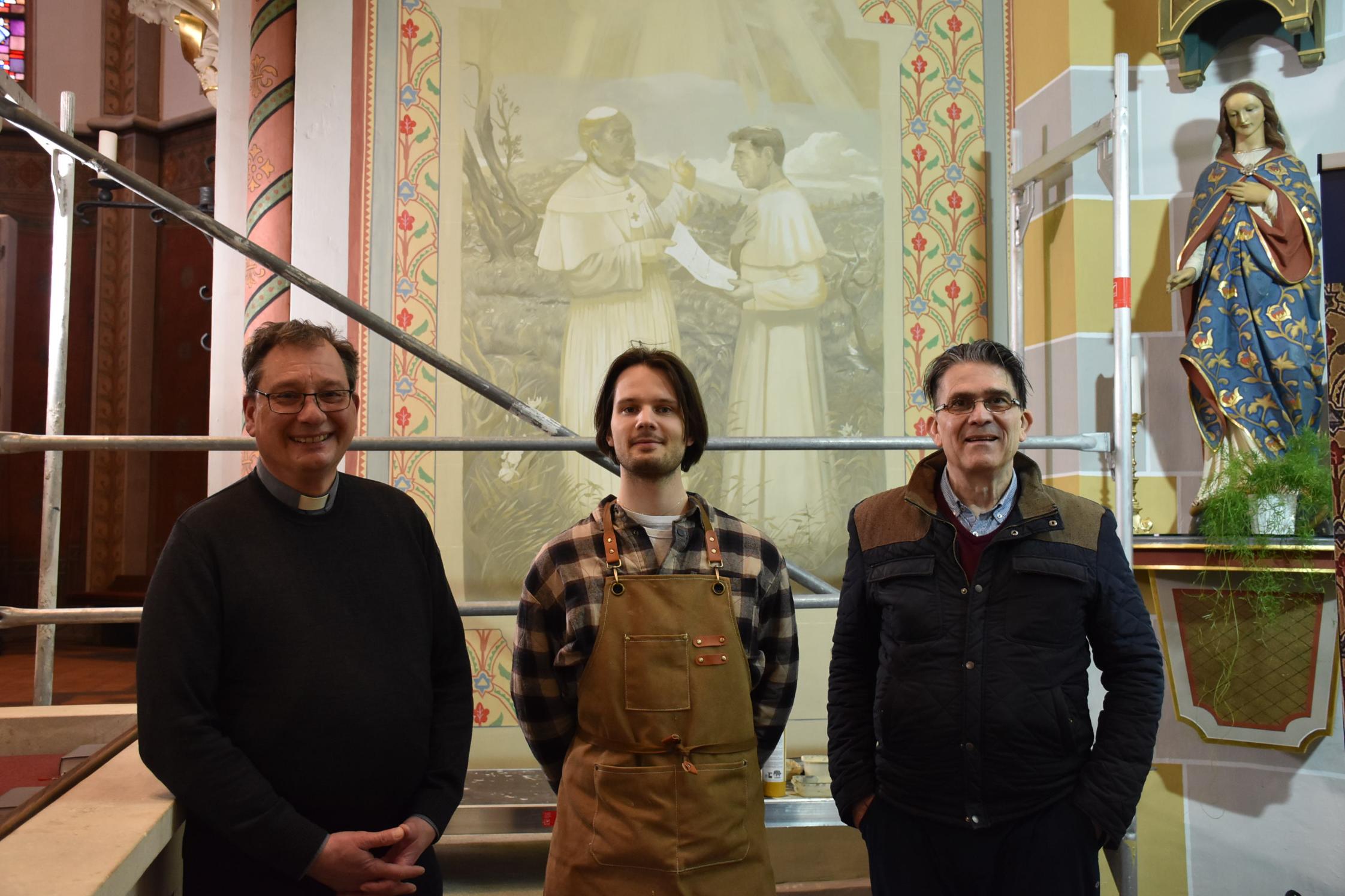 Pfarrer Peter Leick, Jonas Hammen und Patrik Feltes (von links) vor dem Bildnis, das bis Ende des Monats fertiggestellt sein soll.