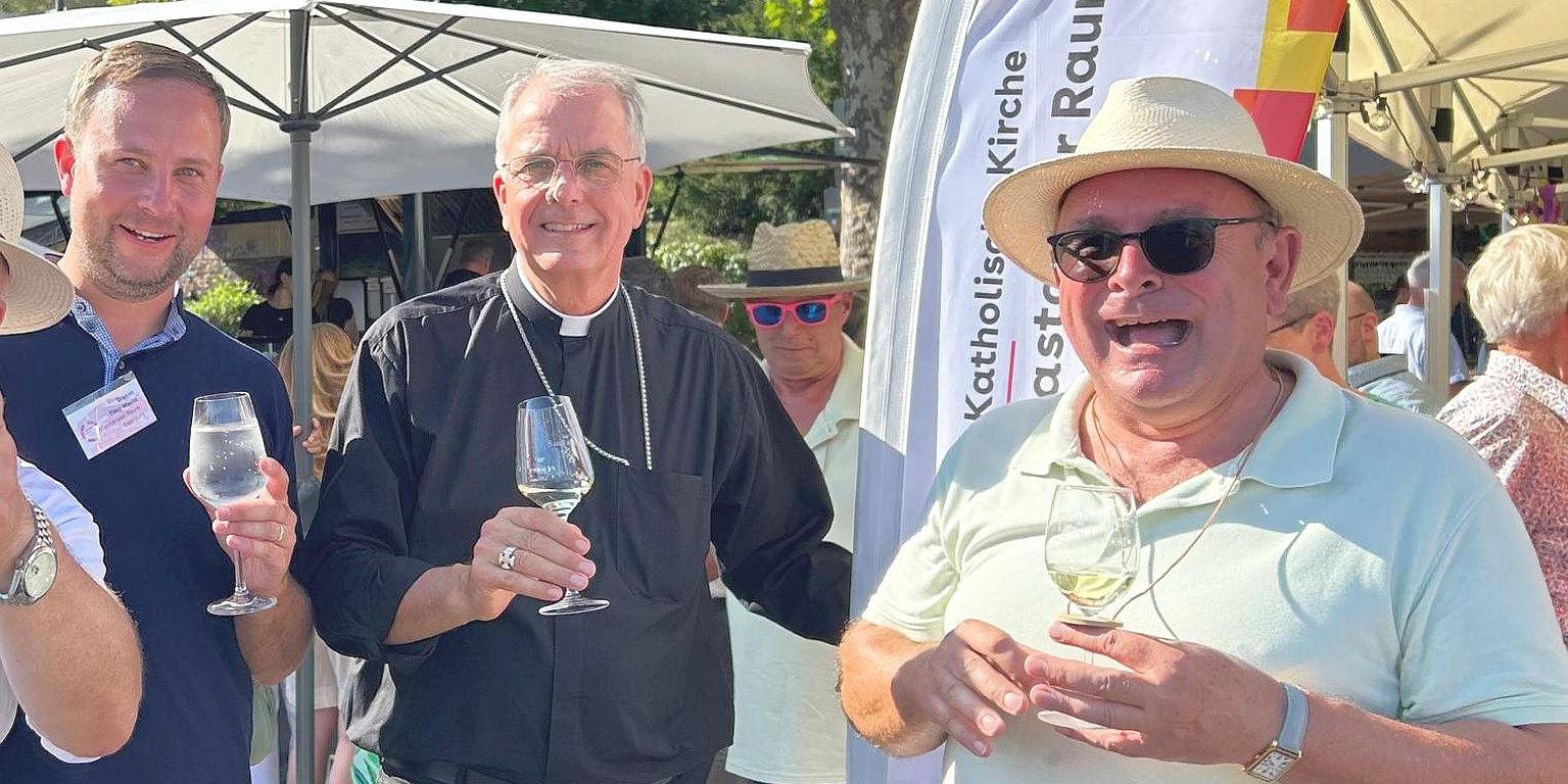 Drei Personen darunter  Weihbischof Jörg Michael Peters (Mitte) bei der Weinprobe.