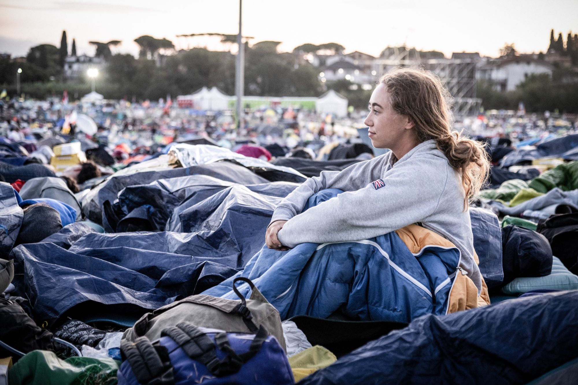 Am Morgen nach der Gebetsnacht beim Weltjugendtreffen 2025 in Rom: Eine junge Frau sitzt in ihrem Schlafsack und blickt über das Gelände.