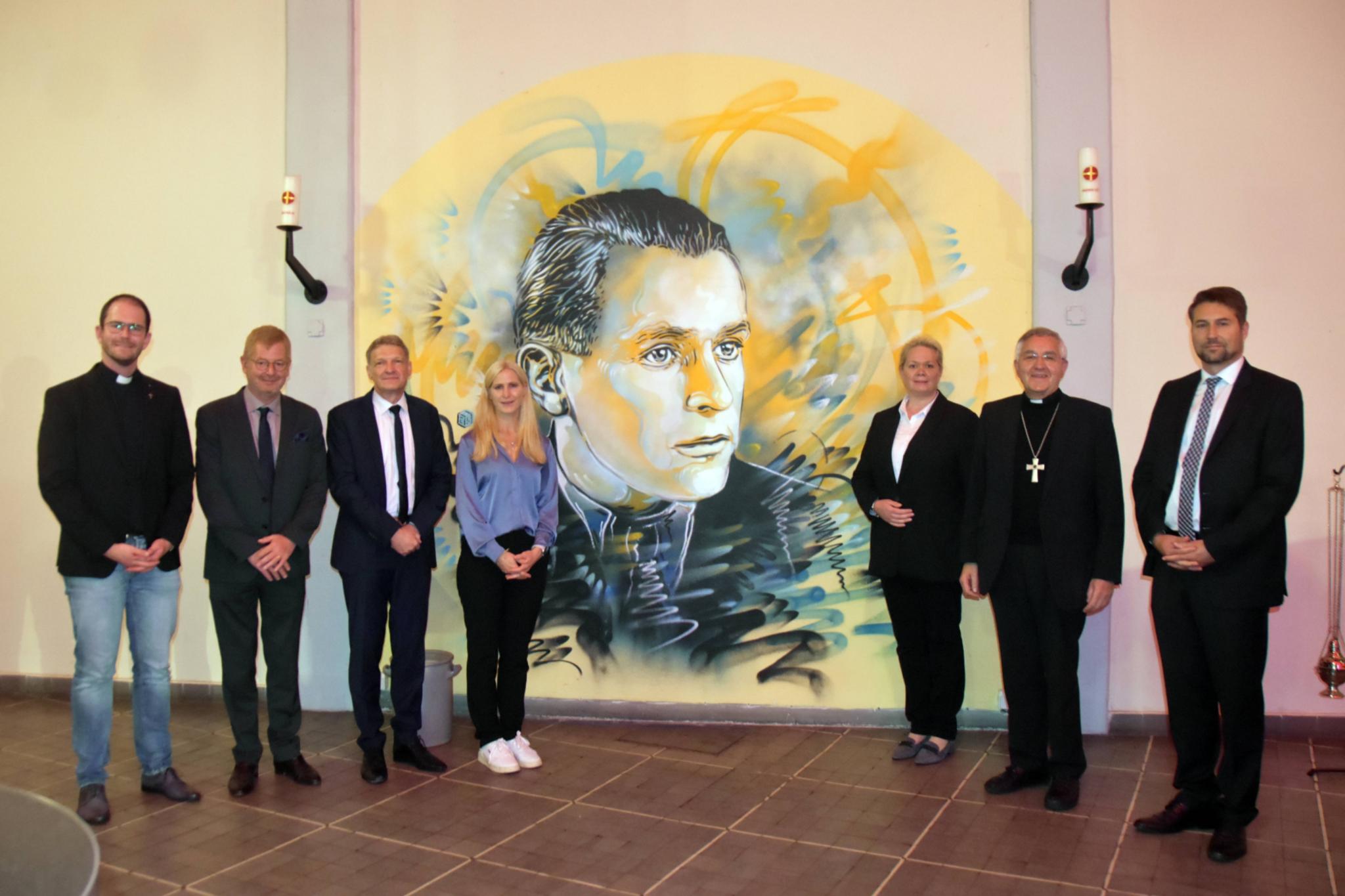 Thomas Hufschmidt, Sebastién Girard, Stephan Toscani, Juliane Baez, Heike Becker, Franz Josef Gebert und Uwe Conradt (von links) vor dem Porträt Willi Grafs des Streetart-Künstlers Christian Guémy in der Jugendkirche.