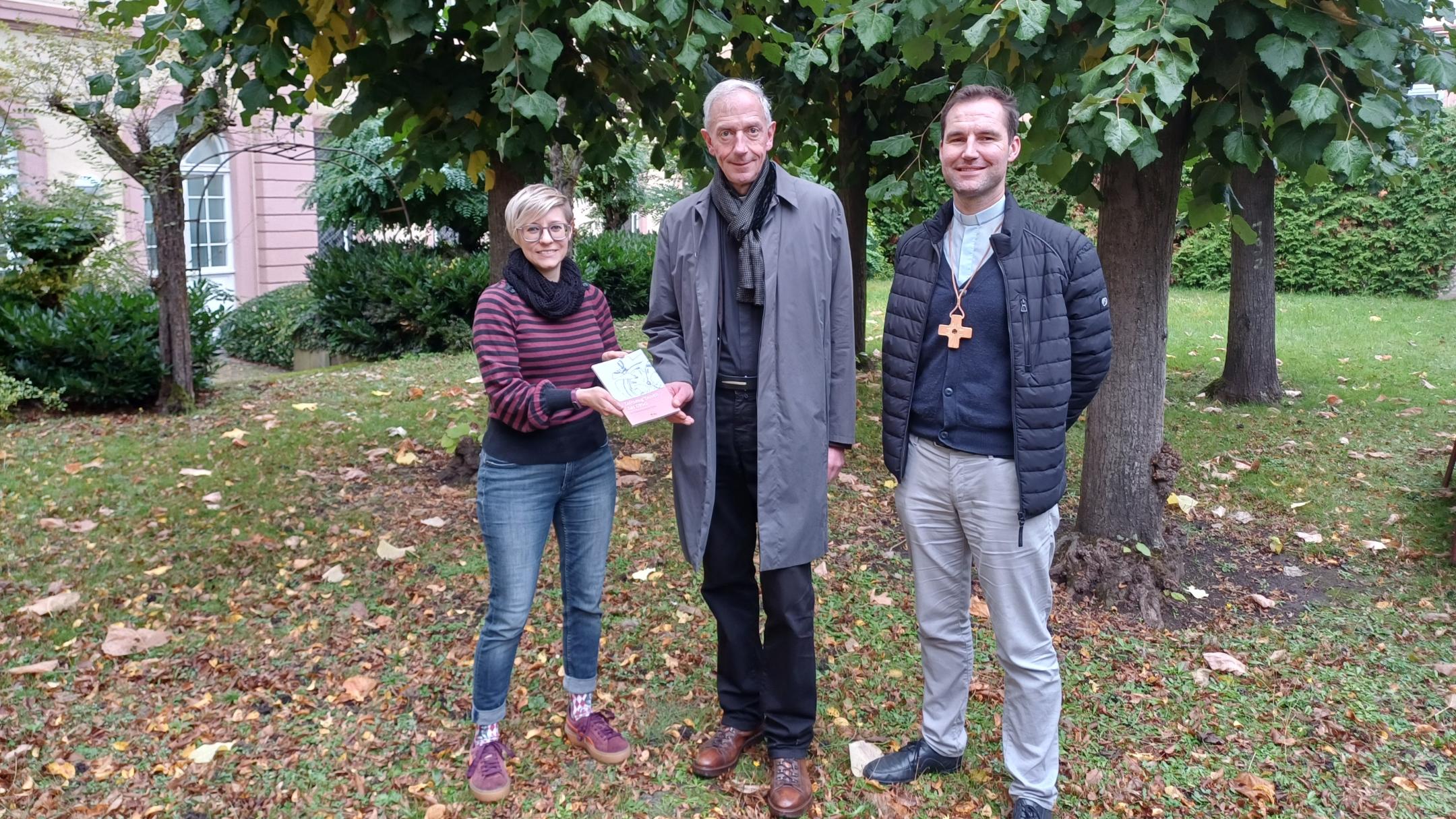 Julia Lehn und Peter Zillgen (rechts) übergeben ein Exemplar des Zeitzeugen-Bandes an Domkapitular und Interviewpartner Benedikt Welter.