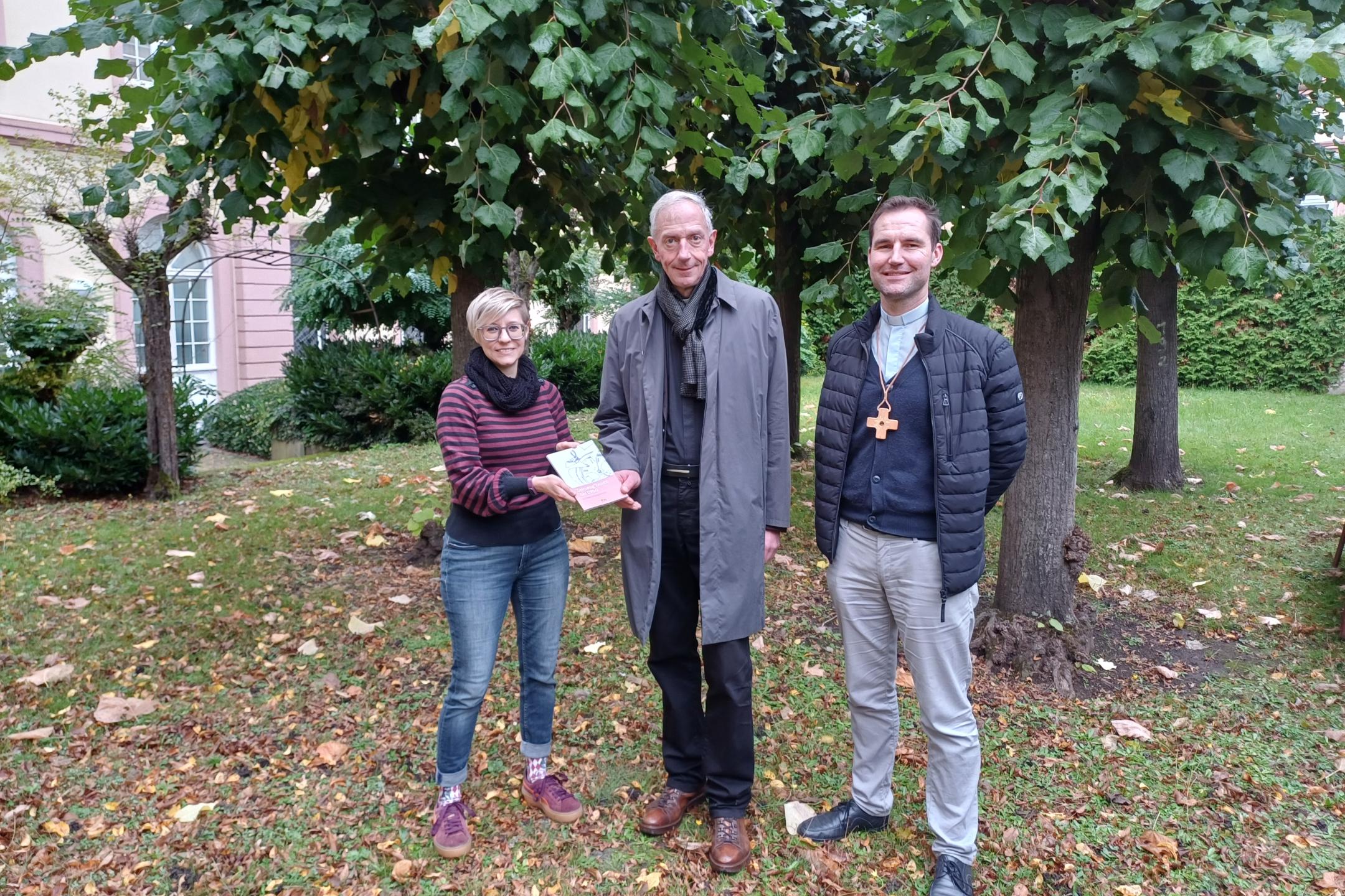 Julia Lehn und Peter Zillgen (rechts) übergeben ein Exemplar des Zeitzeugen-Bandes an Domkapitular und Interviewpartner Benedikt Welter.