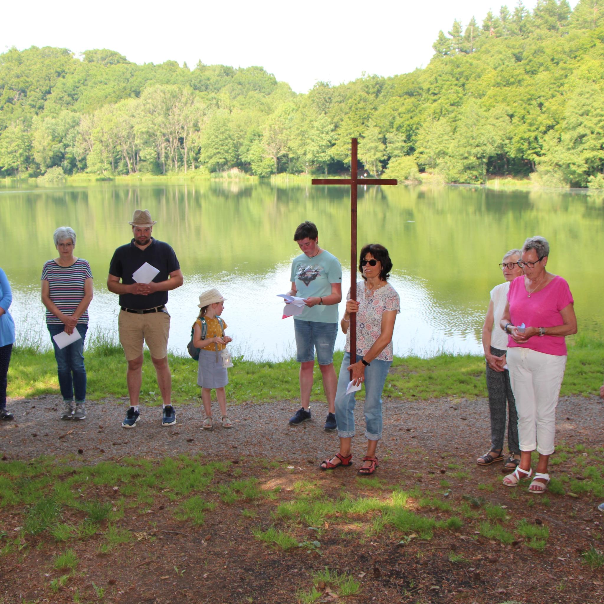 Menschen stehen mit einem Kreuz vor einem See