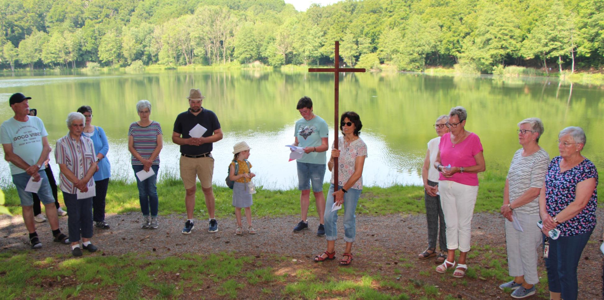 Menschen stehen mit einem Kreuz vor einem See