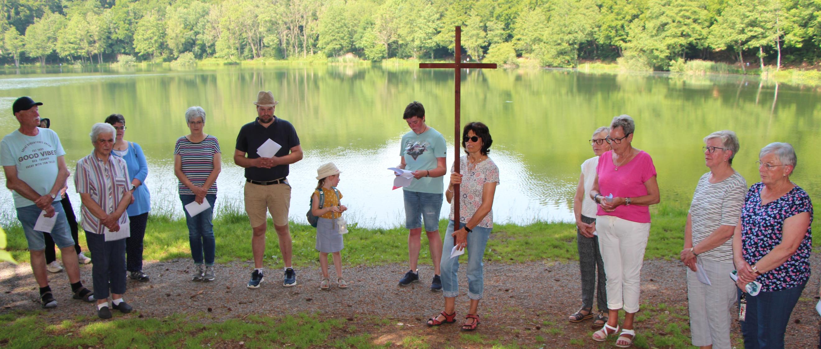 Menschen stehen mit einem Kreuz vor einem See