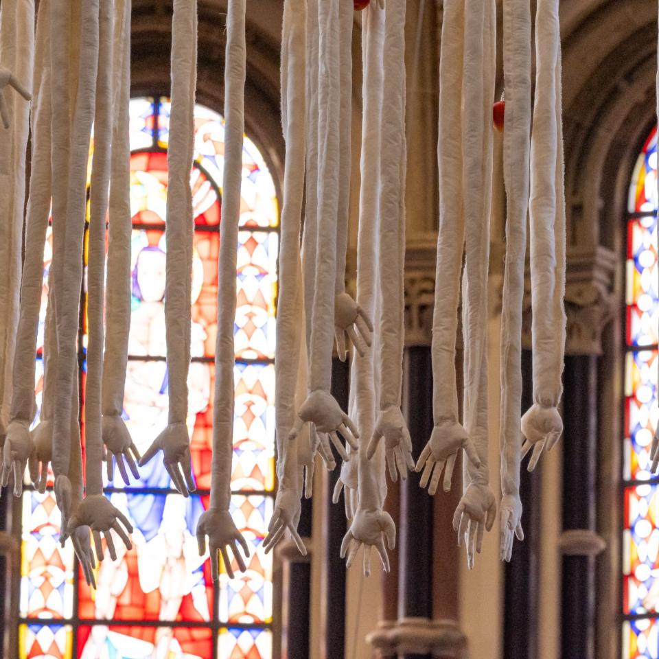 Das Kunstwerk „Mensch“ von Barbara Gröbl zeigt Arme und Hände, die vom Kirchengewölbe herabhängen, geschaffen aus Leinen, mit Äpfeln.