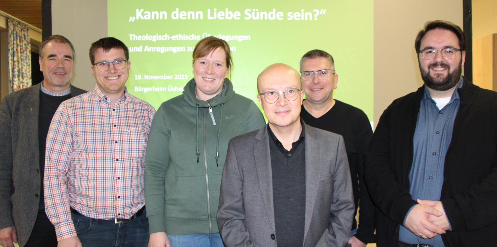 Sechs Personen stehen vor einer grünen Leinwand und lächeln in die Kamera