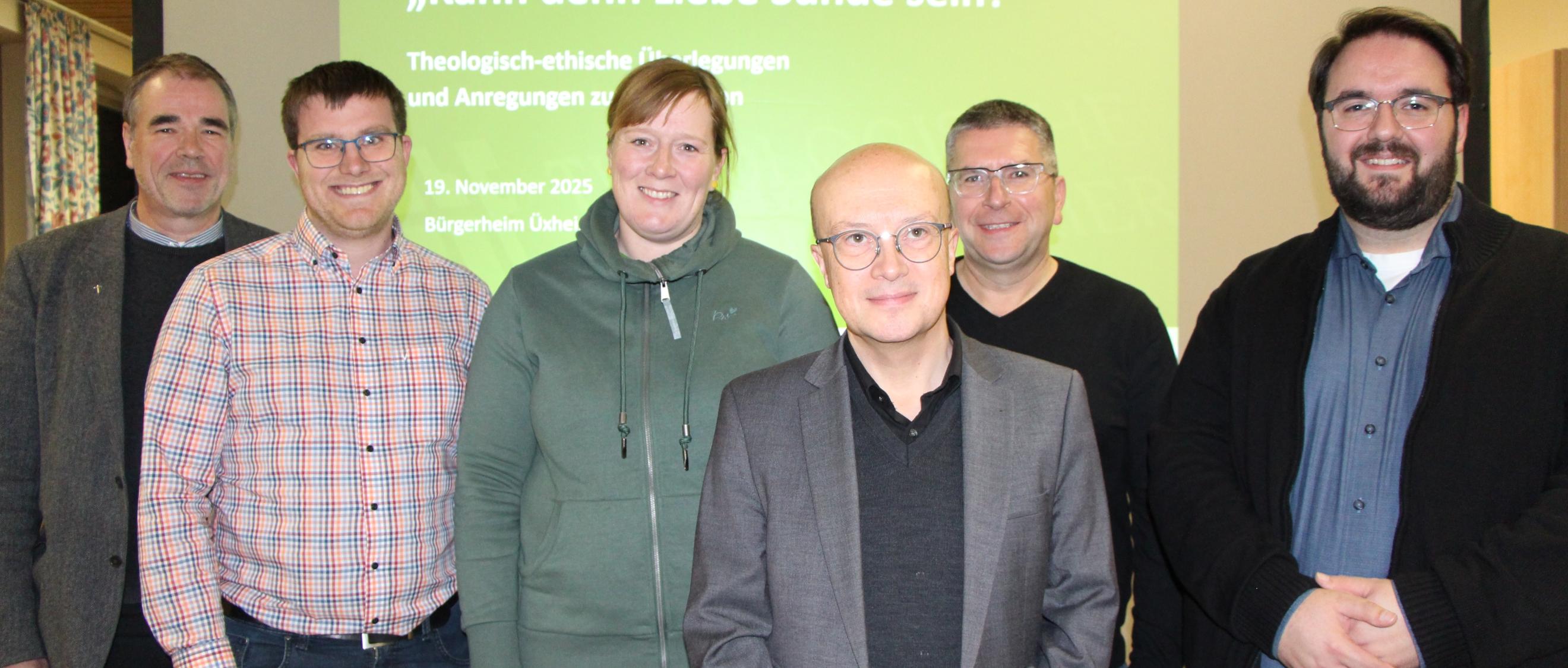 Sechs Personen stehen vor einer grünen Leinwand und lächeln in die Kamera