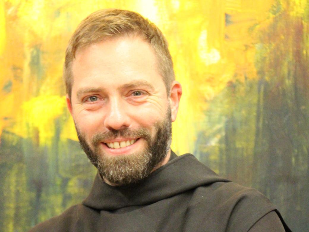 Ein Mönch in Brauer Kutte lächelt in die Kamera mit verschränkten Armen