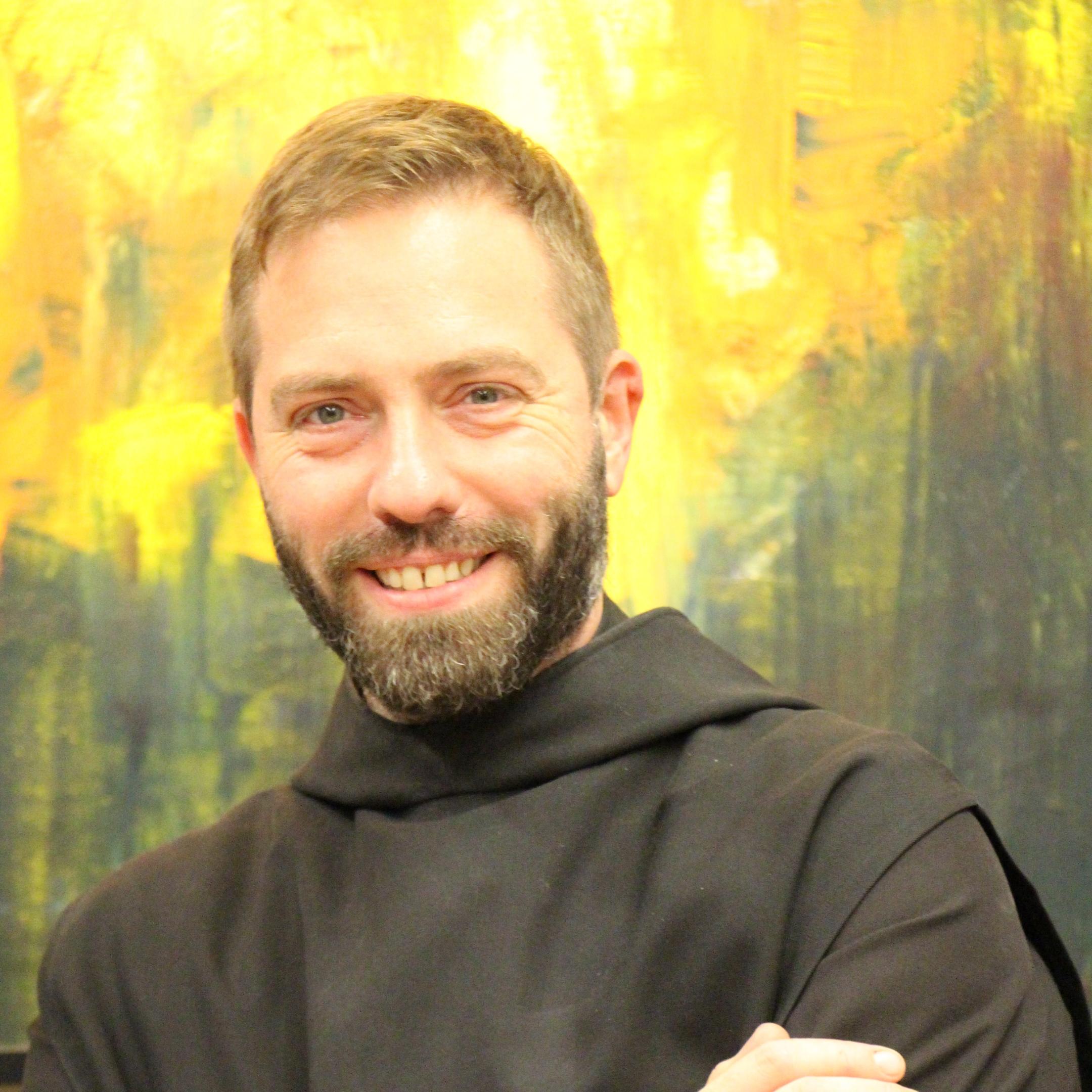 Ein Mönch in Brauer Kutte lächelt in die Kamera mit verschränkten Armen