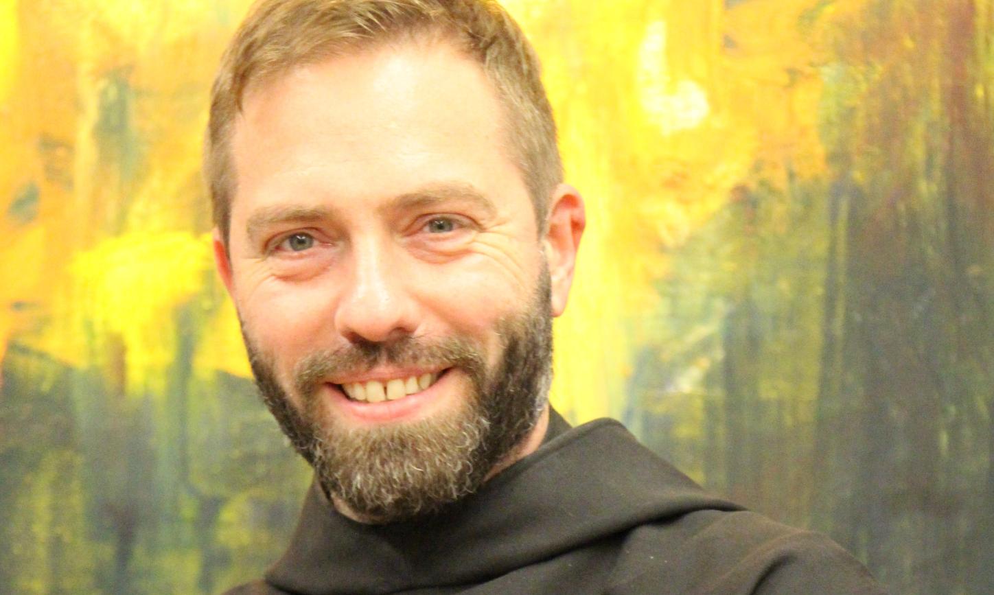 Ein Mönch in Brauer Kutte lächelt in die Kamera mit verschränkten Armen