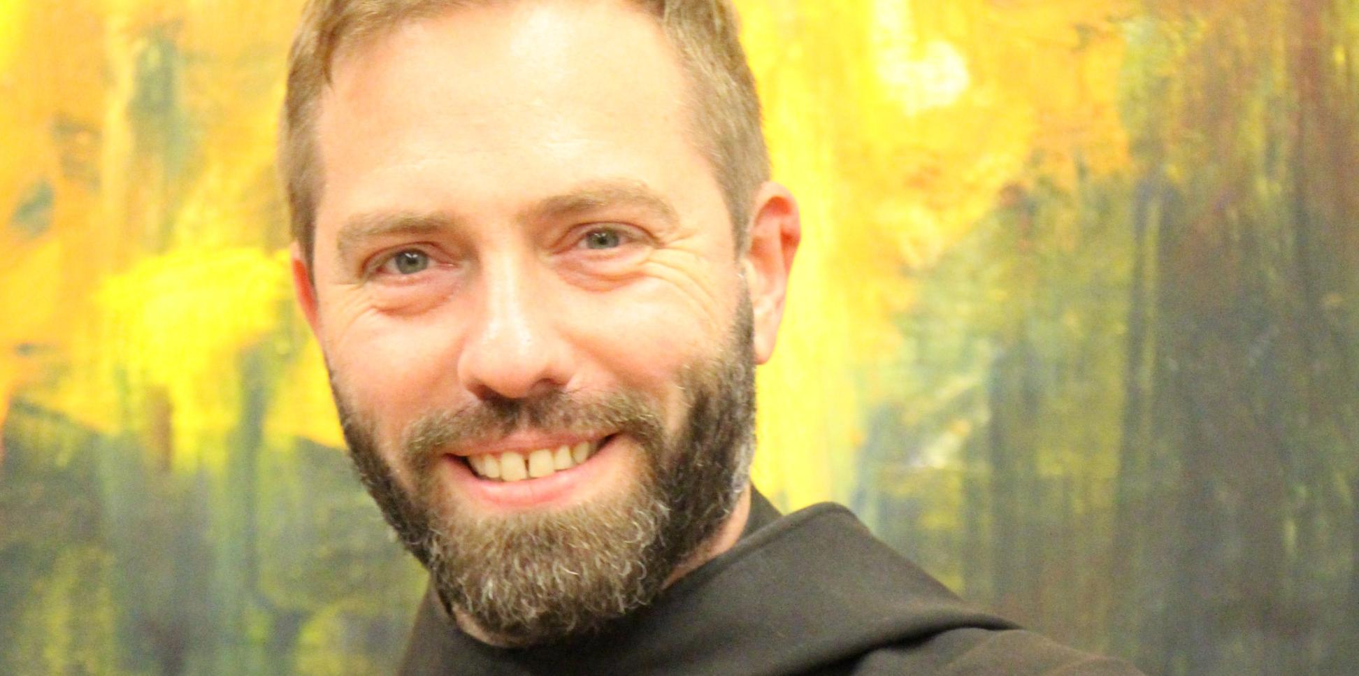 Ein Mönch in Brauer Kutte lächelt in die Kamera mit verschränkten Armen