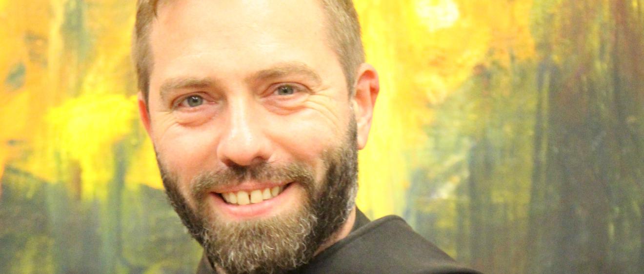 Ein Mönch in Brauer Kutte lächelt in die Kamera mit verschränkten Armen