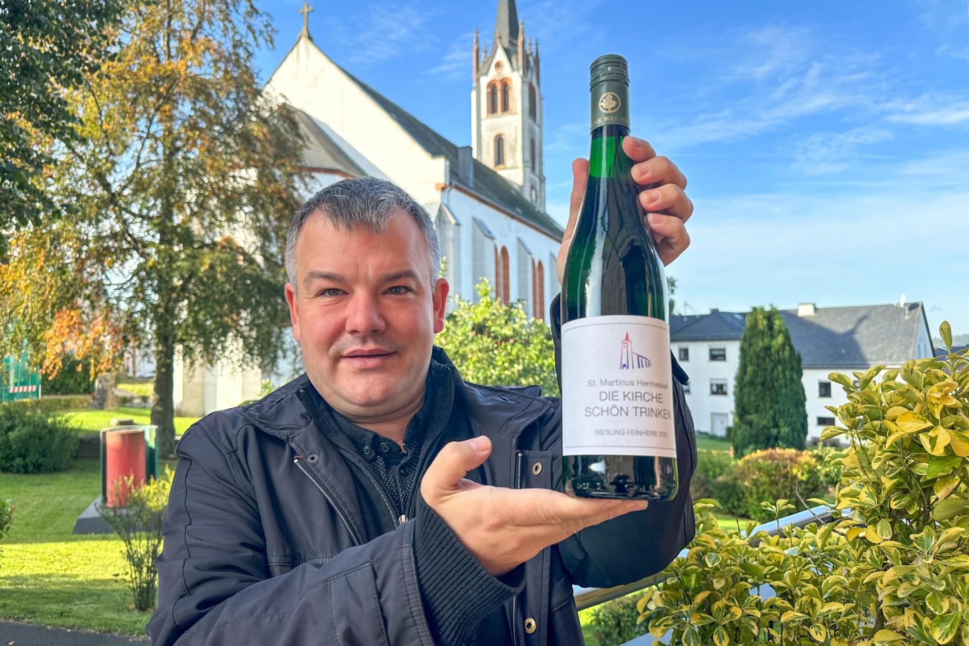 Dechant Christian Heinz präsentiert vor der St. Martinus-Kirche eine der 5000 Flaschen des Charity-Weins.